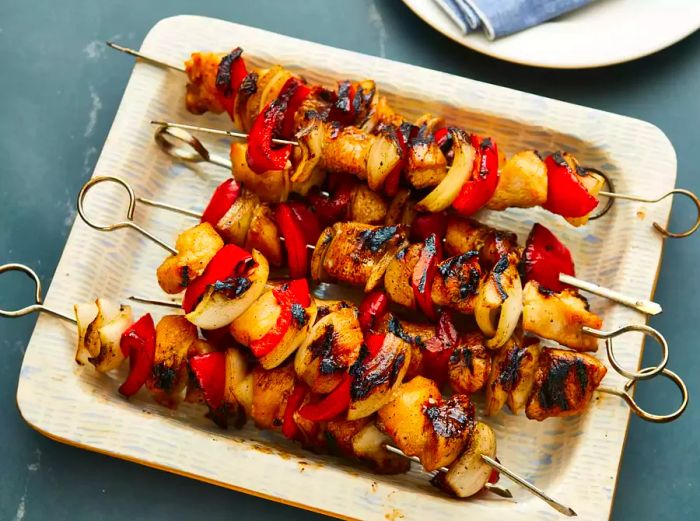 A top-down view of a plate filled with chicken kabobs, onions, and red peppers.