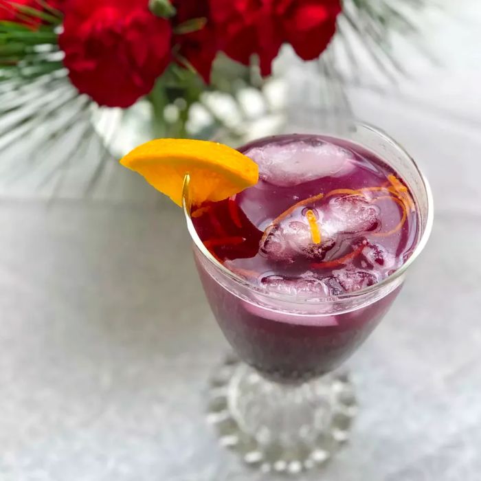 A blueberry fizz mocktail garnished with an orange slice.