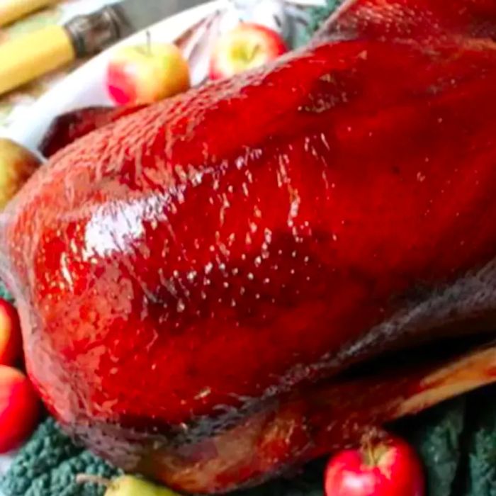 An overhead view of a beautifully golden roast goose, served on a decorative platter surrounded by vibrant kale and small apples.