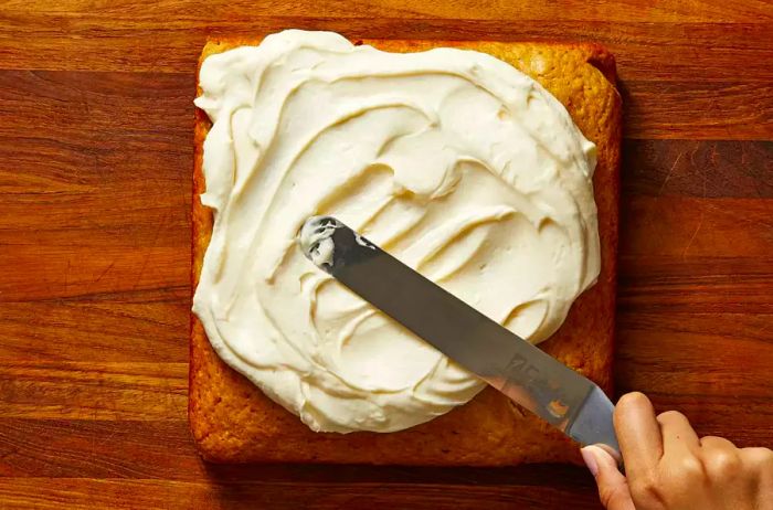 A square cake being decorated with frosting