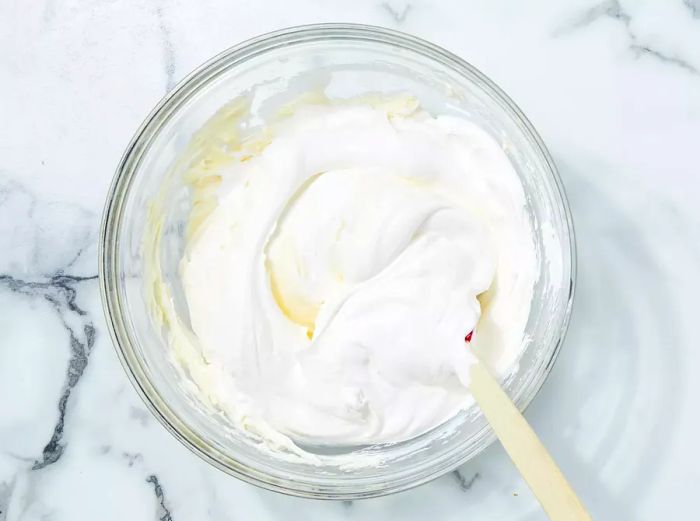 An overhead shot of whipped cream being folded into cream cheese.