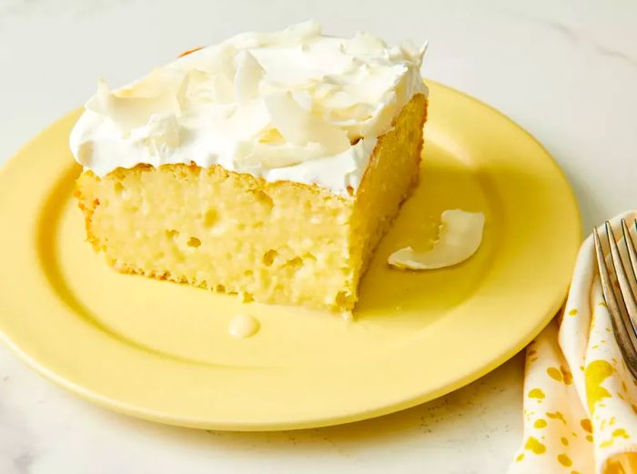 High-angle view of a slice of coconut poke cake served on a yellow plate.