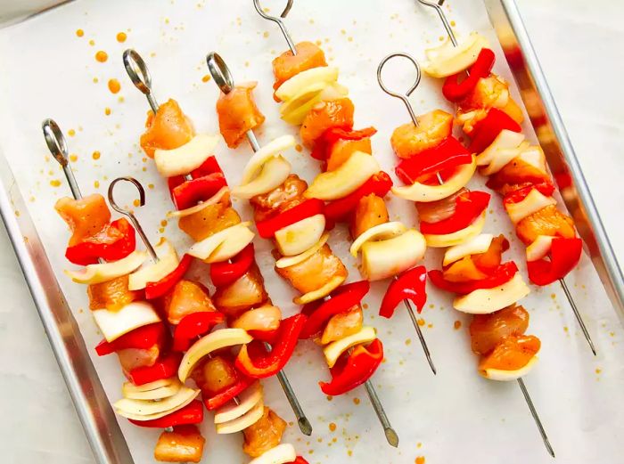 Chunks of chicken and vegetables alternately threaded onto skewers, arranged on a baking sheet.