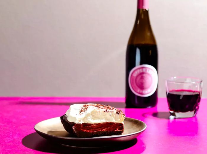 A slice of rich chocolate pie with a glass of wine in the background