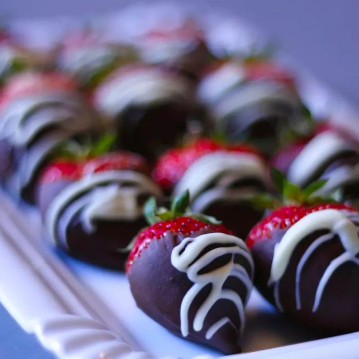 A white square plate filled with plump strawberries dipped in rich chocolate and drizzled with a delicate white chocolate swirl.