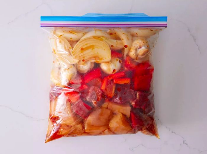 A large ziplock bag filled with beef, chicken, and sliced vegetables marinating