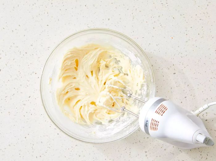 Cream cheese frosting blending together in a mixing bowl.