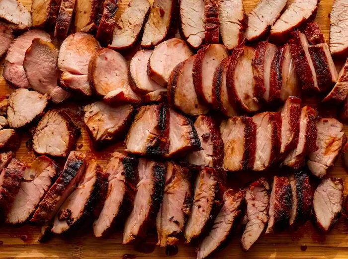 An overhead shot of sliced char siu on a wooden cutting board.