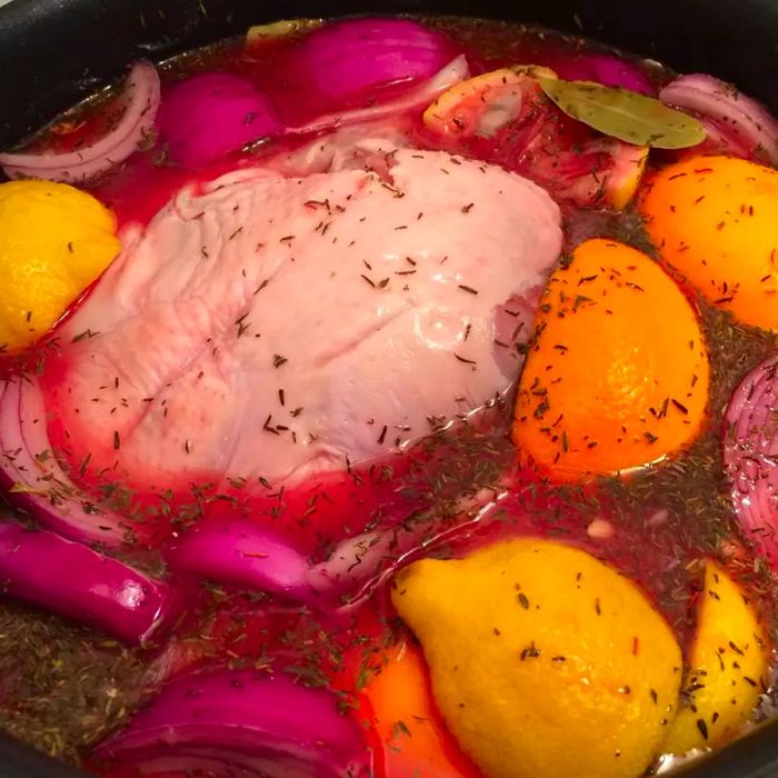 A raw turkey soaking in a brine mixture with oranges, lemons, and purple onions