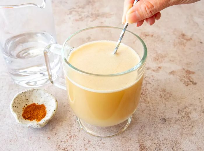 A person stirring the hot buttered rum in a glass.