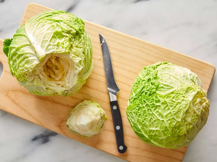 A top-down view showing two cabbages being cored on a cutting board.