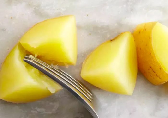 Using a fork to check the tenderness of boiled potatoes by testing for doneness