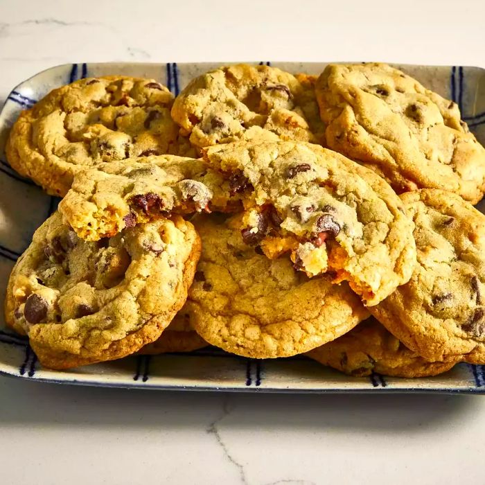 A close-up of a stack of the best-ever chocolate chip cookies, with one broken in half to reveal its gooey center.