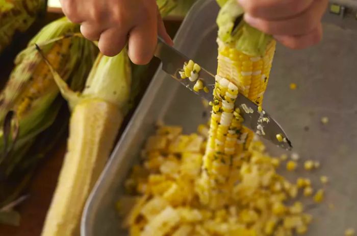 Corn being cut over a baking dish