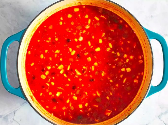 An overhead view of black beans, cooked chicken, and corn simmering in a tomato-based broth in a large pot.