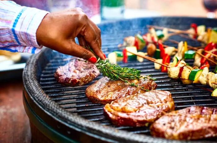 Woman basting meat on barbecue with fresh herbs