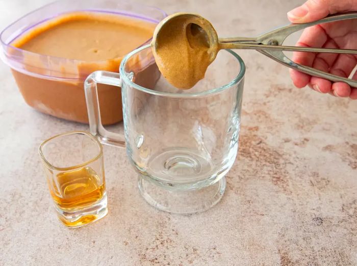 A person scooping the hot buttered rum mixture into a glass.