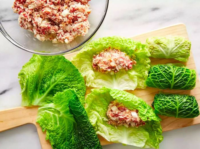 A high-angle shot of cabbage rolls on a cutting board being filled with the stuffing mixture.