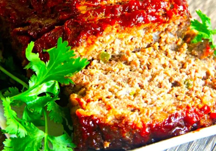 A beautifully glazed meatloaf served on a white ceramic platter, sliced with a garnish of fresh celery leaves.