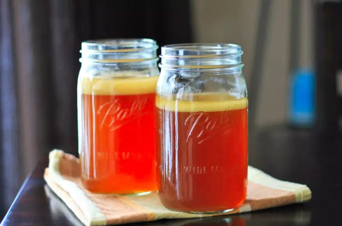 Two mason jars filled with rich, amber-colored stock