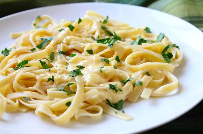 Fettuccine Alfredo served on a white plate, topped with freshly chopped Italian parsley