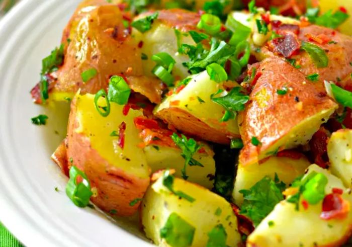 Close-up shot of grilled potato salad garnished with crispy bacon, fresh herbs, and scallions