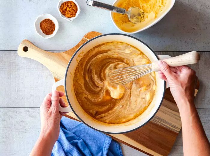 A person whisking a hot buttered rum mixture in a pot.