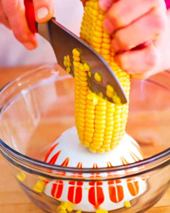 Corn being sliced off the cob into a bowl