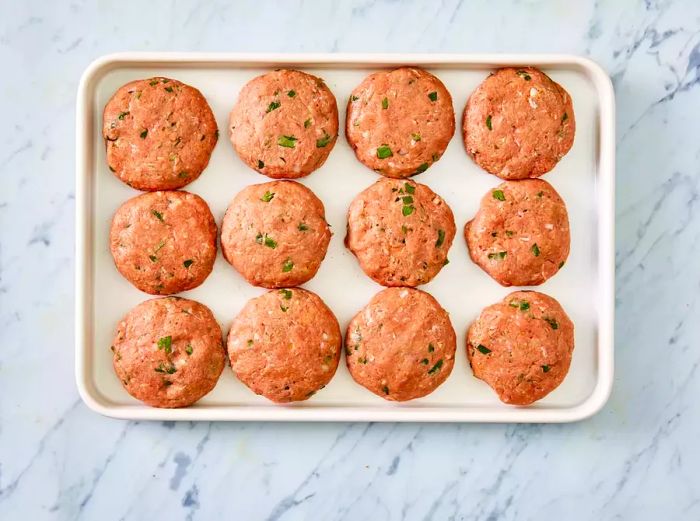 A top-down view of twelve turkey burger patties resting on a baking sheet.