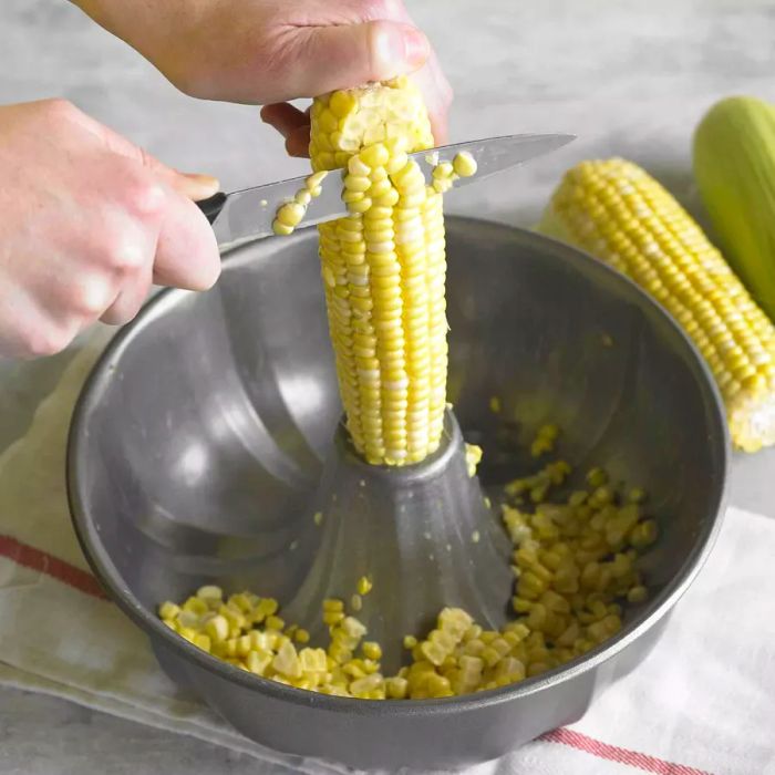 Corn being sliced off the cob over a bundt pan