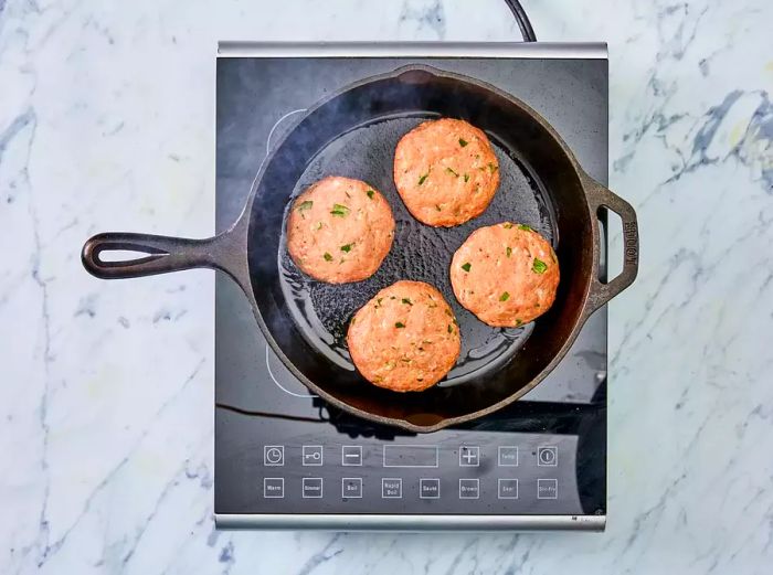 A top-down view of turkey burger patties cooking in a skillet.