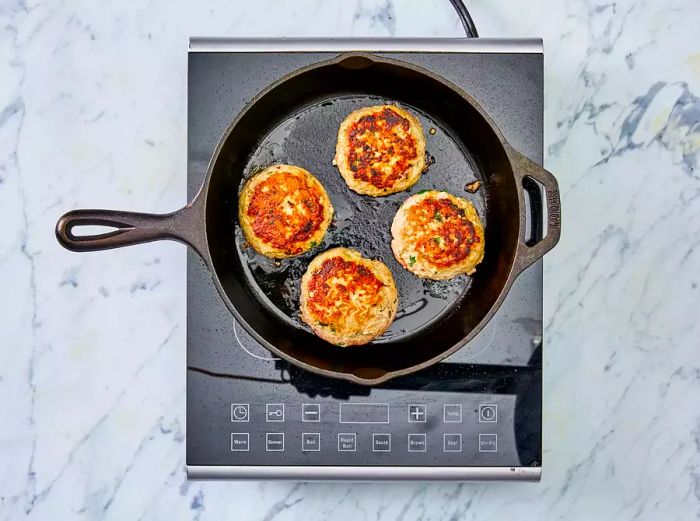 Turkey burgers sizzling in a skillet.