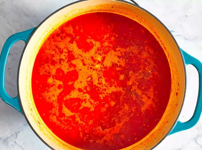 An overhead view of crushed tomatoes and broth simmering in a large pot.