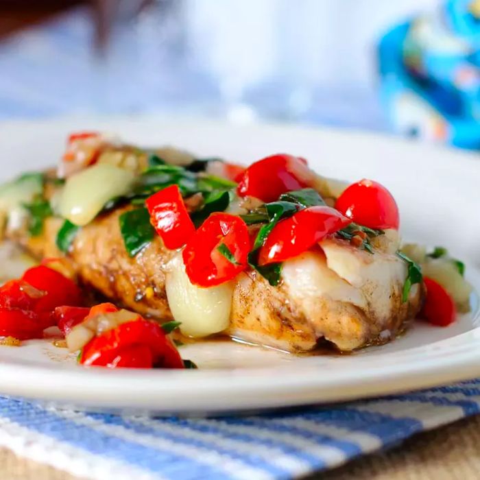 A plate of perfectly grilled cod topped with fresh spinach and juicy tomatoes