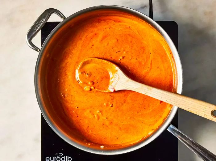 A large pan of rich, creamy tomato sauce being stirred with a wooden spoon