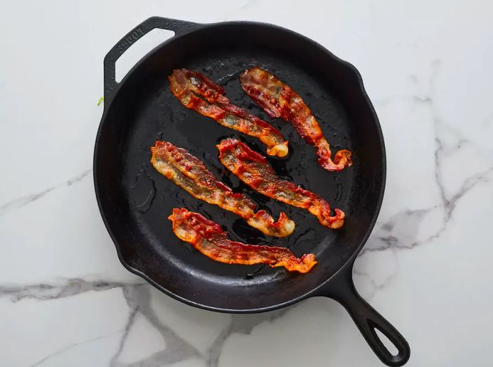 A top-down view of crispy bacon in a cast iron skillet.