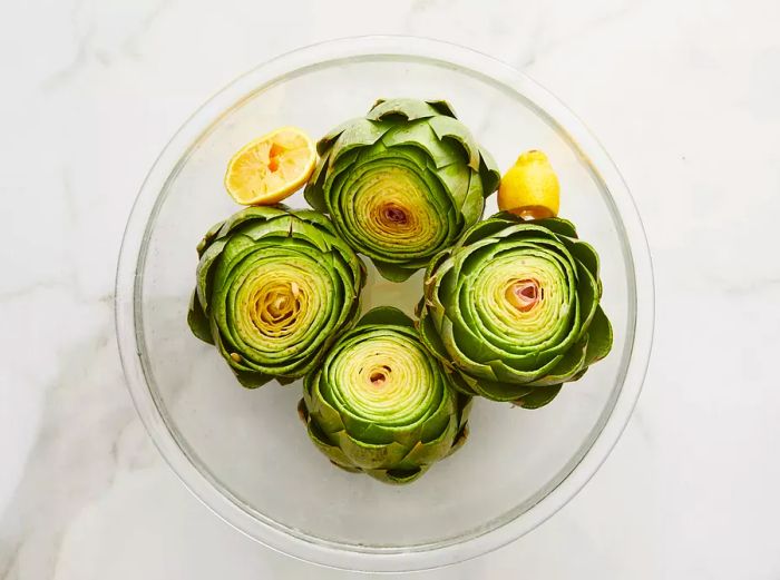 Artichokes arranged stem side down in a bowl, topped with a drizzle of lemon juice.