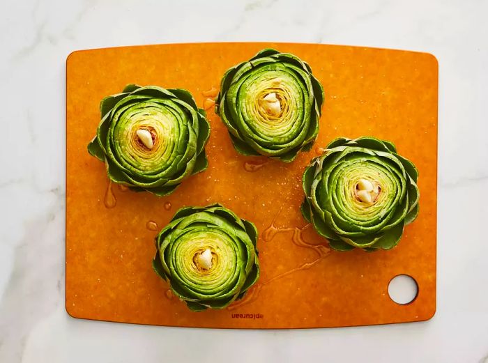 Garlic cloves inserted into the center of each artichoke, with olive oil drizzled on top.