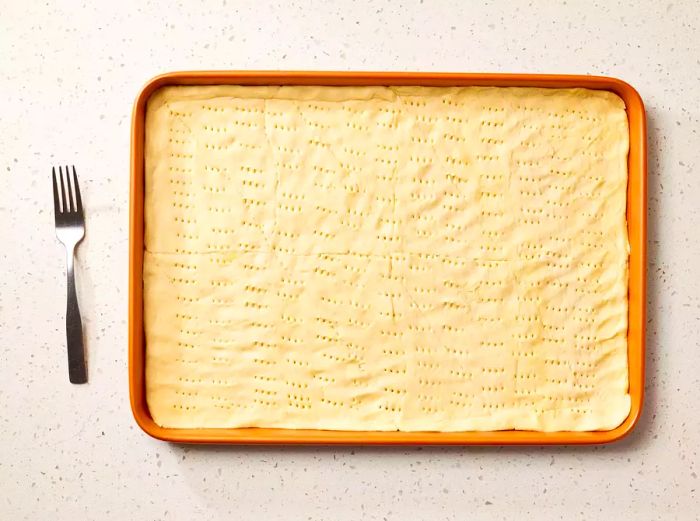 A jelly roll pan lined with crescent roll dough, punctured evenly with a fork.