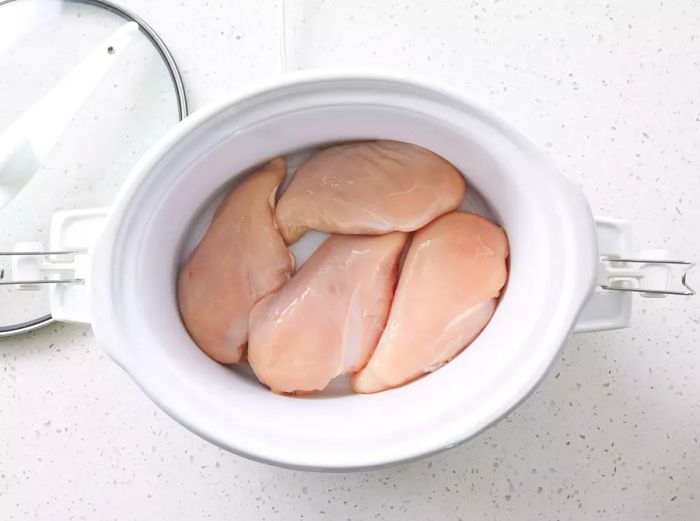 A slow cooker filled with four chicken breasts.