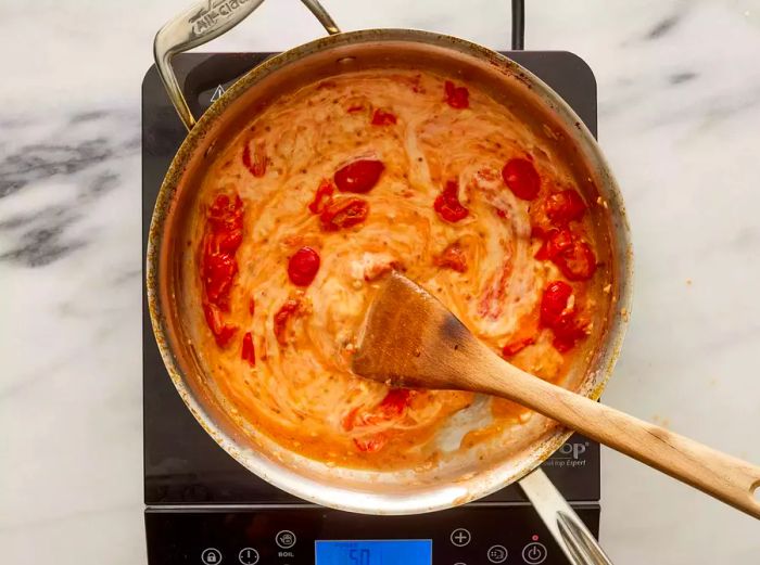 A pan with grape tomatoes and melted cheese being stirred with a wooden spoon