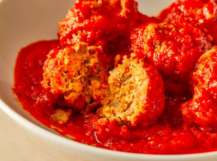 A mid-angle shot of a bowl of meatballs, with one cut in half to reveal its interior