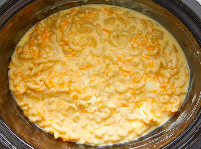 A top-down view of eggs, condensed soup, milk, shredded cheese, and macaroni noodles all layered in a crockpot.