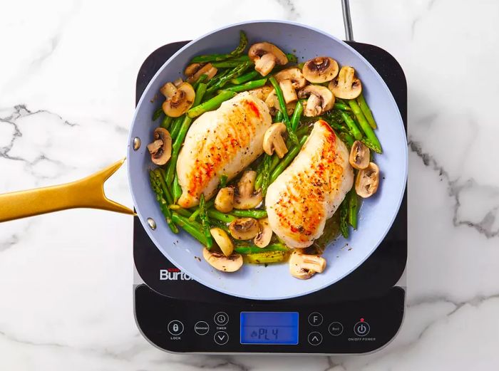 Golden-browned chicken, asparagus, and mushrooms sizzling in a skillet.