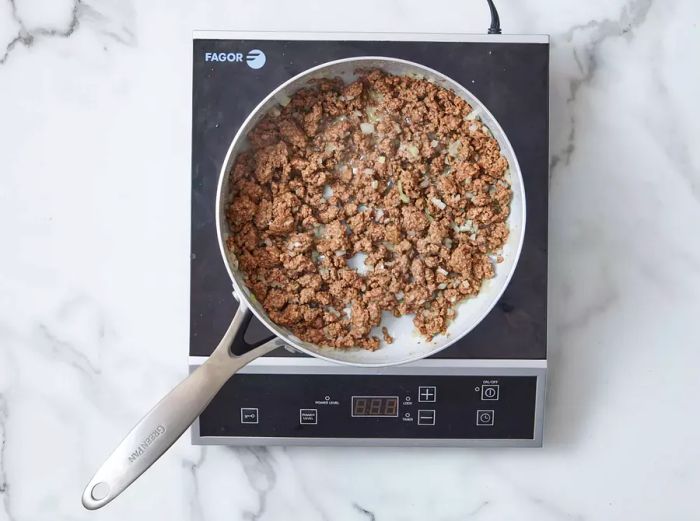 A skillet filled with cooked ground beef and chopped onions