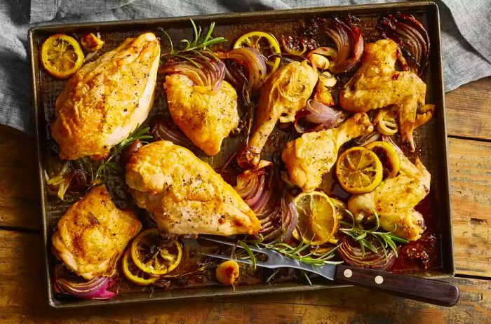 A roasted chicken breast on a sheet pan with lemon and rosemary