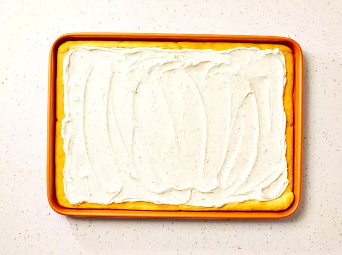 A jelly roll pan featuring a crescent roll crust, generously topped with a creamy ranch-flavored cream cheese spread.