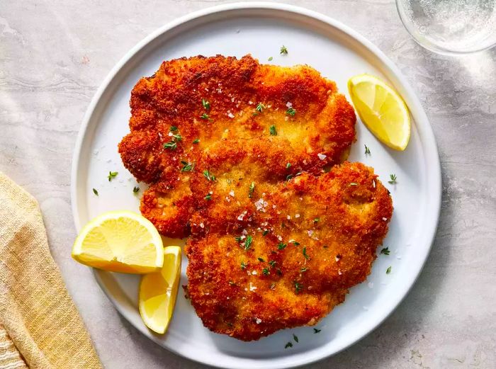 An overhead shot of a perfectly golden-brown, crispy pork schnitzel garnished with lemon slices.