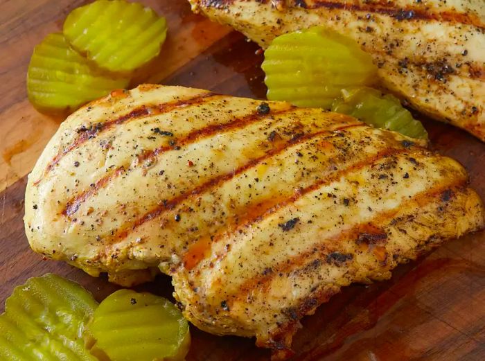 Close-up of a grilled pickle-brine chicken breast served with pickles