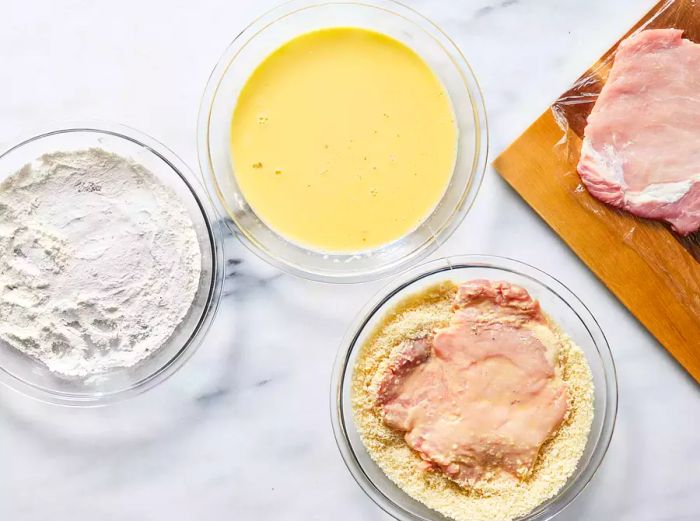 Chicken being coated in breadcrumbs.